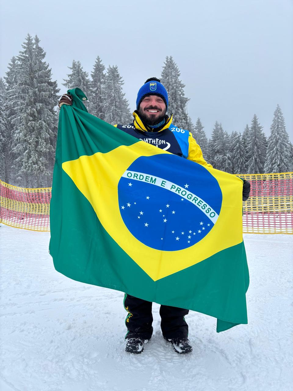 Dr. Lucas Garbulha segurando a bandeira do Brasil em competição de neve paralímpica